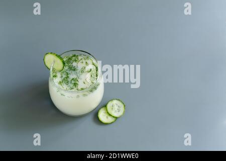 Ayran in a glass glass with dill and cucumbers on a gray background. Fermented product concept. Copy space. Selective focus Stock Photo