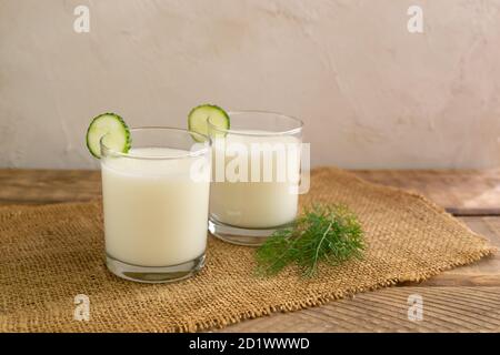 Two glasses with Ayran with a cucumber on a wooden background. Fermented product concept. Copy space. Horizontal orientation. Stock Photo
