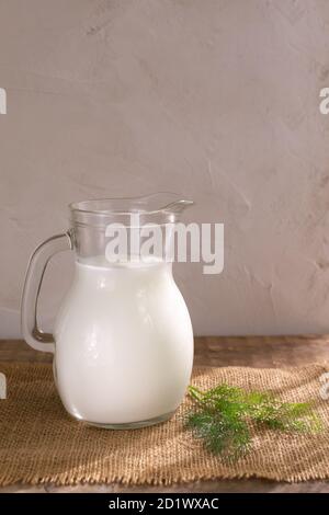 Glass jug with Ayran drink and a sprig of dill on a wooden background. Fermented product concept. Vertical orientation. Copy space. Stock Photo