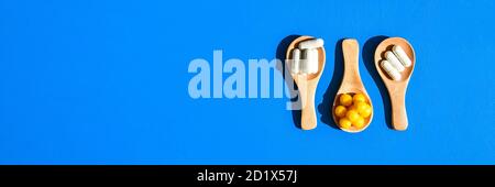 Pills and capsules on wooden spoons on blue background. Hard light and shadows. Copy space. Vitamins prebiotics probiotics. Drug dose. Stock Photo