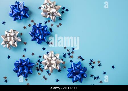 creative pattern with shiny bow from bright ribbon on blue background. Trendy silver,blue ribbon. Stylish metallic bows, New year 2021.Advertising Stock Photo