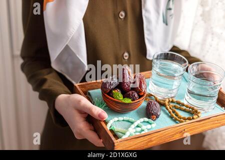 A female hand holds a tray with dates, and water and a rosary - hthe things used to break the fast at sunset during the Muslim holy month of Ramadan. Stock Photo