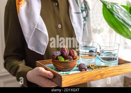 A female hand holds a tray with dates, and water and a rosary - hthe things used to break the fast at sunset during the Muslim holy month of Ramadan. Stock Photo