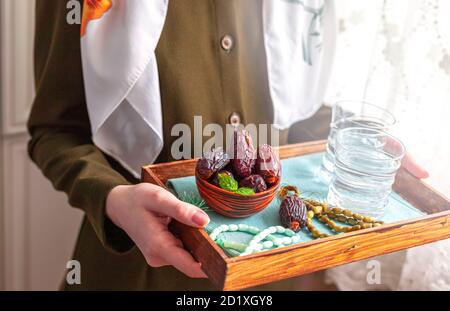 A female hand holds a tray with dates, and water and a rosary - hthe things used to break the fast at sunset during the Muslim holy month of Ramadan. Stock Photo