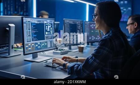 Smart Female IT Programer Working on Desktop Computer in Data Center System Control Room. Team of Young Professionals Doing Code Programming Stock Photo