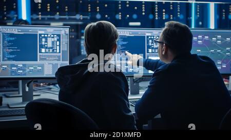 Two Professional IT Programers Discussing Blockchain Data Network Architecture Design and Development Shown on Desktop Computer Display. Working Data Stock Photo