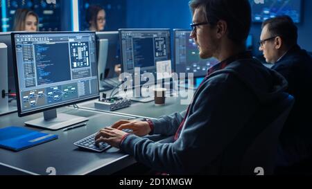 Smart Male IT Programer Working on Desktop Green Mock-up Screen Computer in Data Center System Control Room. Team of Young Professionals Programming Stock Photo