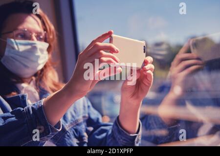 A tourist in a medical mask on her face takes a trip on a phone camera. Travel by public transport during the quarantine coronavirus Stock Photo