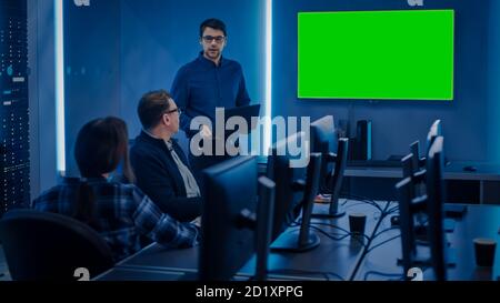 Team of Professional IT Developers Have a Meeting, Speaker Talks about About New Concepts, On Wall TV has Green Mock-up Screen. Concept: Software Stock Photo