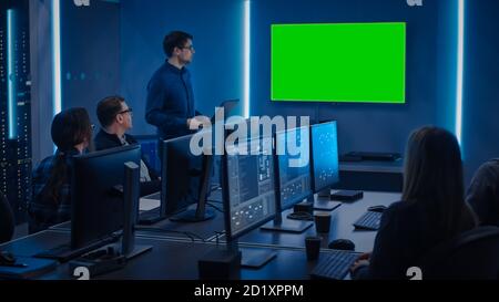 Team of Professional IT Developers Have a Meeting, Speaker Talks about About New Concepts, On Wall TV has Green Mock-up Screen. Concept: Software Stock Photo