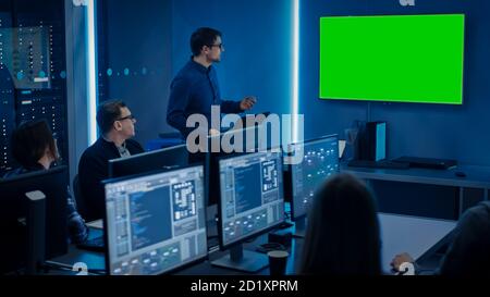 Team of Professional IT Developers Have a Meeting, Speaker Talks about About New Concepts, On Wall TV has Green Mock-up Screen. Concept: Software Stock Photo