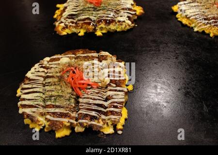 Closeup of Okonomiyaki, Japanese pizza is being cooked on the pan or teppan. Stock Photo