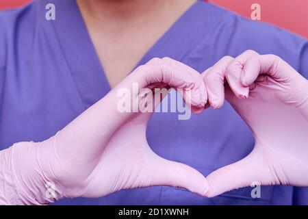The medic shows the heart sign with his fingers, close-up. Doctor's hands in medical gloves with the sign of love for patients, concept. Stay home. Stock Photo
