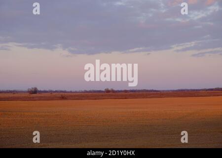 Cloudy evening sky over an empty agricultural field. Bright sunset landscape. Stock Photo