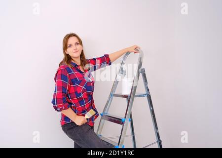 Woman painter in a plaid shirt stands on a stepladder, copy space Stock Photo