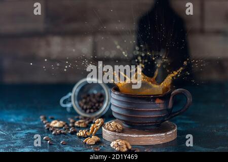 Splash of iced coffee in handmade ceramic mug and roasted beans and nuts on a dark background. Stock Photo