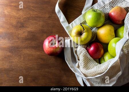 Eco mesh bag with apples supplies on a wooden background. Food delivery in eco-friendly packaging, zero waste. Stock Photo