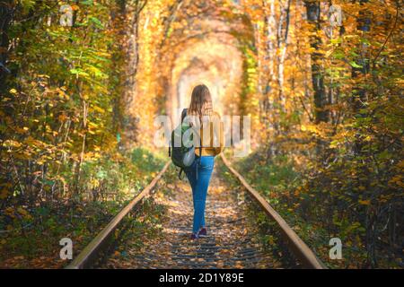 Young woman walking on the railroad in tunnel of trees in autumn Stock Photo