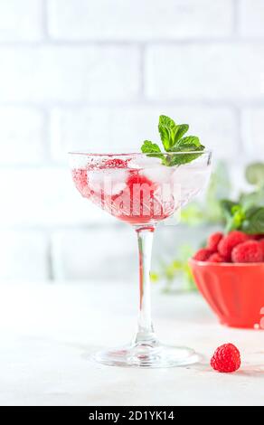 Raspberry lemonade with mint and ice in a glass on a light concrete background. Stock Photo