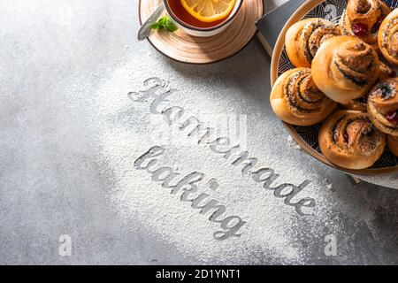 The inscription on the flour Homemade baking. Homemade buns with poppy seeds, tools and baking products on a light background. Stock Photo