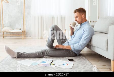 Focused man sitting on floor using phone drinking coffee Stock Photo