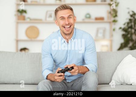 Excited emotional guy sitting on sofa playing video games Stock Photo