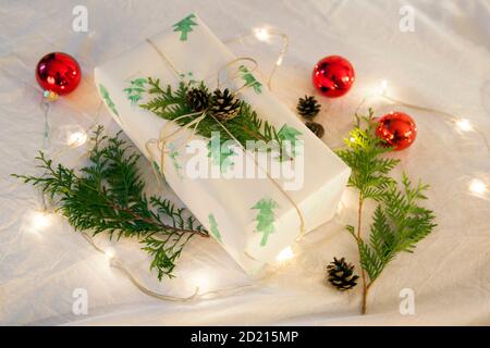 Christmas present wrapped in old fashioned paper against wrinkled white cloth. Christmas balls, pinecones and fir. Stock Photo