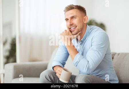 Pensive man sitting on sofa drinking coffee Stock Photo
