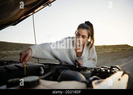 Stressed young caucasian teenager fixing car after breaking down on empty highway. Stock Photo