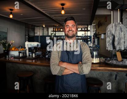 Smiling waiter standing with cross-arms happily working in cafe  Stock Photo