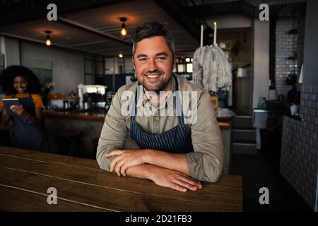 Handsome coffee shop owner smiling while sitting at table in funky coffee shop. Stock Photo