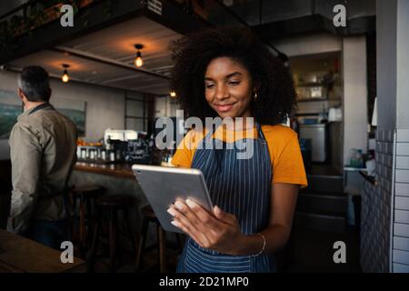 Smiling waitress choosing meal option for customer scrolling on digital tablet in trendy cafe  Stock Photo