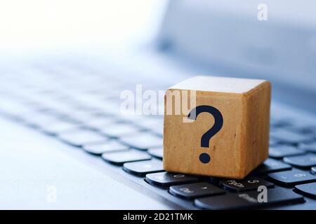 A question mark on a wooden cube on a computer keyboard, with a blurred background and shallow depth of field. Stock Photo