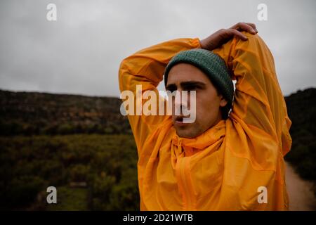 Concentrating young male athlete stretching shoulder with elbow before long distance run up mountain trail in cloudy weather Stock Photo