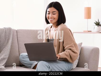 Asian woman sitting on couch and working on pc Stock Photo
