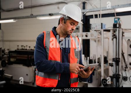 Caucasian engineer scrolling on digital tablet standing in factory Stock Photo