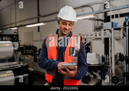 Smiling engineer holding tablet standing in factory Stock Photo