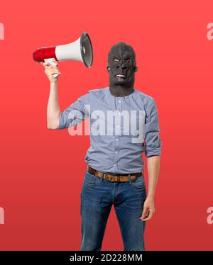 Man wearing gorilla mask holding up megaphone next to head. Isolated cutout on red background. Three quarter length. Stock Photo