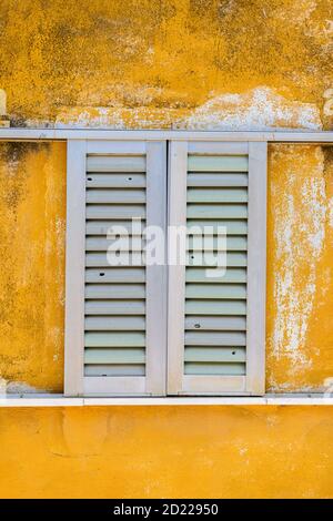 White window shutters on a yellow building Stock Photo