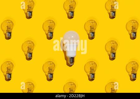 One saving light bulb and many incandescent lamps on a yellow background. Idea concept. Stock Photo