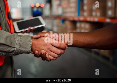 Close up of caucasian an ethnic male co-workers shaking hands after making successful deal in warehouse Stock Photo