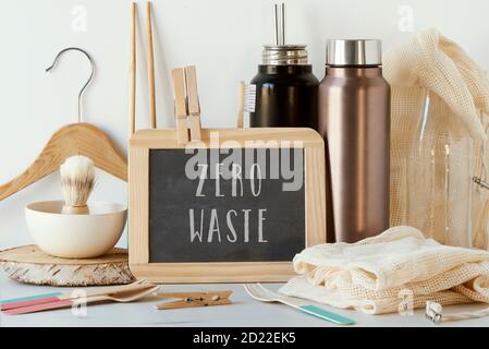 the text zero waste in a chalkboard and a pile of no-plastic sustainable items, such as metal water bottles, a glass bottle, shopping mesh bags or reu Stock Photo
