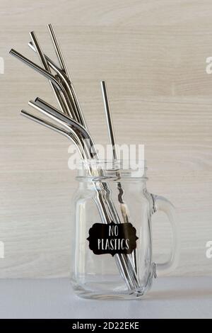 some metal reusable drinking straws with different shapes and lenghts in a handled glass jar, and the text no plastics written in a label attached to Stock Photo