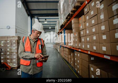 portrait of caucasian male worker typing on digital tablet searching for packages in factory shop Stock Photo