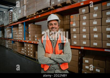 Smiling male worker standing cross-armed happily besides packaged parcels ready for delivery  Stock Photo