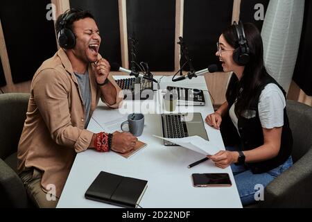 Portait of two cheerful radio hosts, young man and woman laughing while discussing various topics, reading a script, moderating a live show in studio Stock Photo