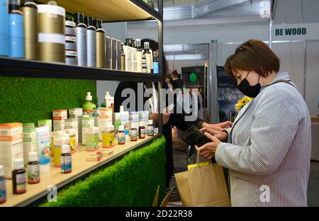 Woman standing in front of a counter with cannabis cosmetics (oil, creams, soaps, conditioners) and giving money to seller. Cannabis fair Stock Photo