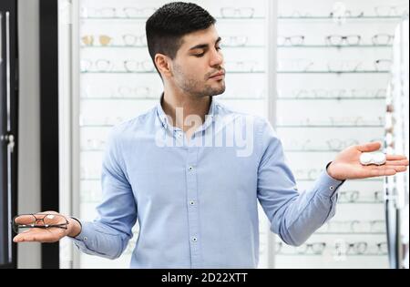 Pensive guy choosing between eyeglasses and contacts Stock Photo