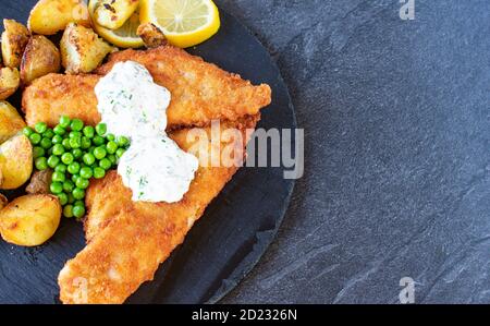 breaded fish fillet with fried potates, peas and tatar sauce on dark background from above with copy space Stock Photo