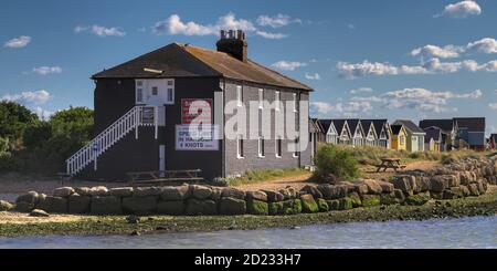 Black House On Mudeford Sand Spit With Beach Huts In Background Taken From Mudeford Quay UK Stock Photo